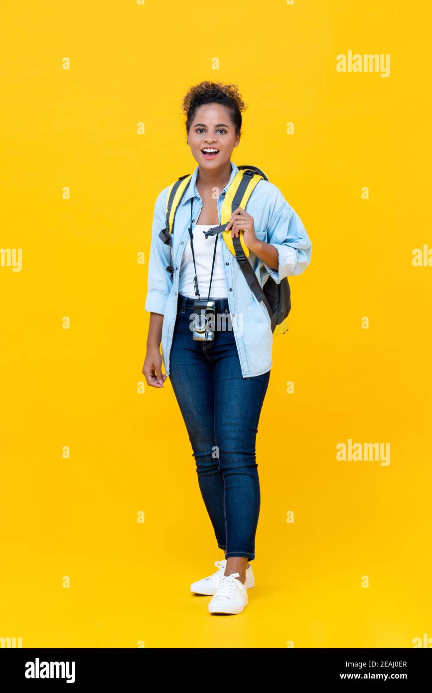 Cuerpo completo de hermosa mujer joven afroamericana sonriente turista backpacker listo para las vacaciones de pie sobre fondo amarillo estudio Foto de stock