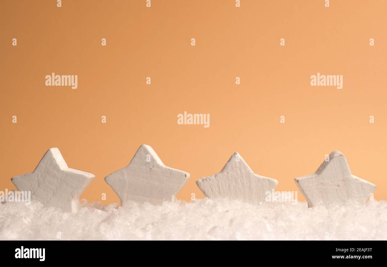Cuatro formas de estrellas de madera blanca con nieve sobre un fondo de papel naranja, espacio para texto en la parte superior Foto de stock