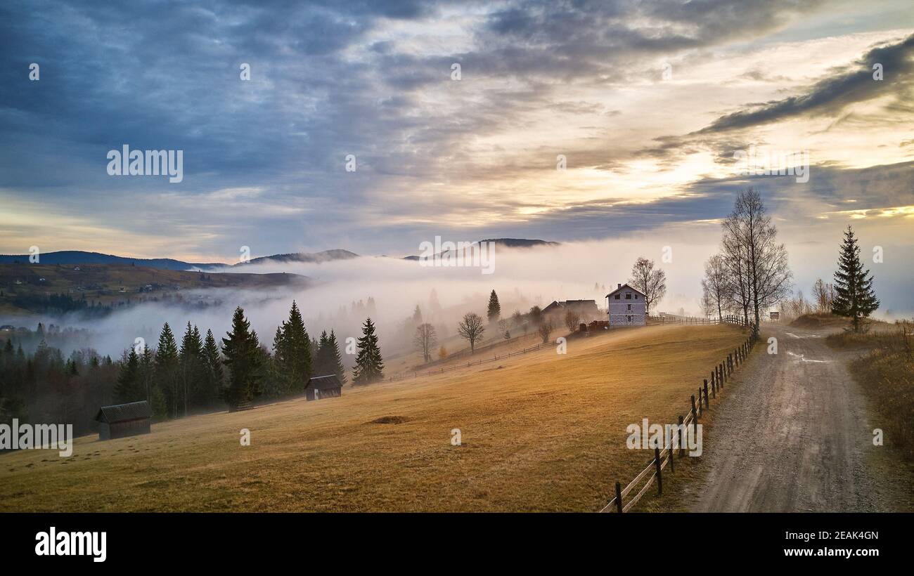 Pueblo alpino. Paisaje rural de otoño. Fría en la mañana de noviembre. Niebla matutina en el valle de montaña Foto de stock
