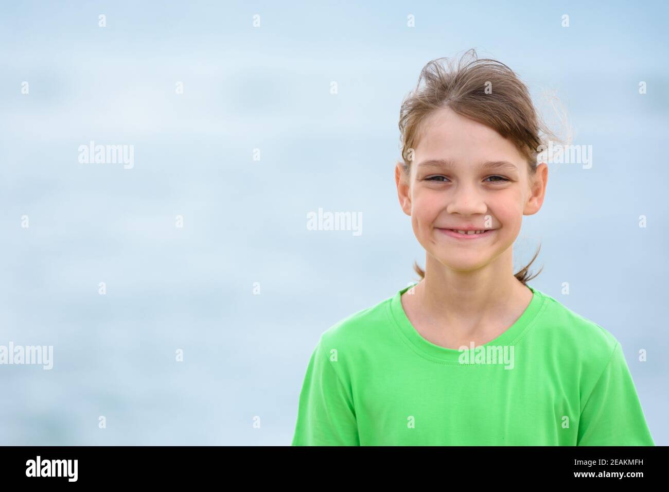 Retrato de una chica feliz de diez años en una camiseta verde sobre el fondo del mar Foto de stock
