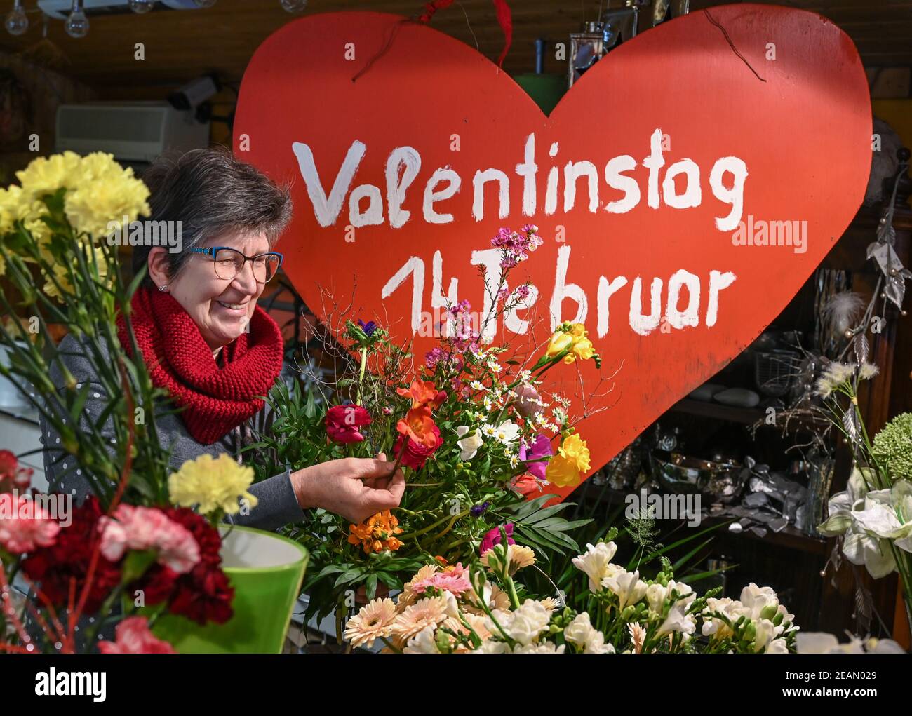 Vevais, Alemania. 10 de febrero de 2021. Carla Hofmann, florista y  propietaria de la floristería, está al lado de un gran corazón con las  palabras "San Valentín 14 de febrero" y ata