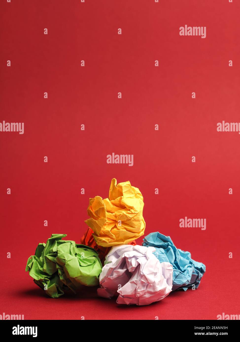 Coloridas bolas de papel arrugadas sobre un fondo rojo de estudio Foto de stock