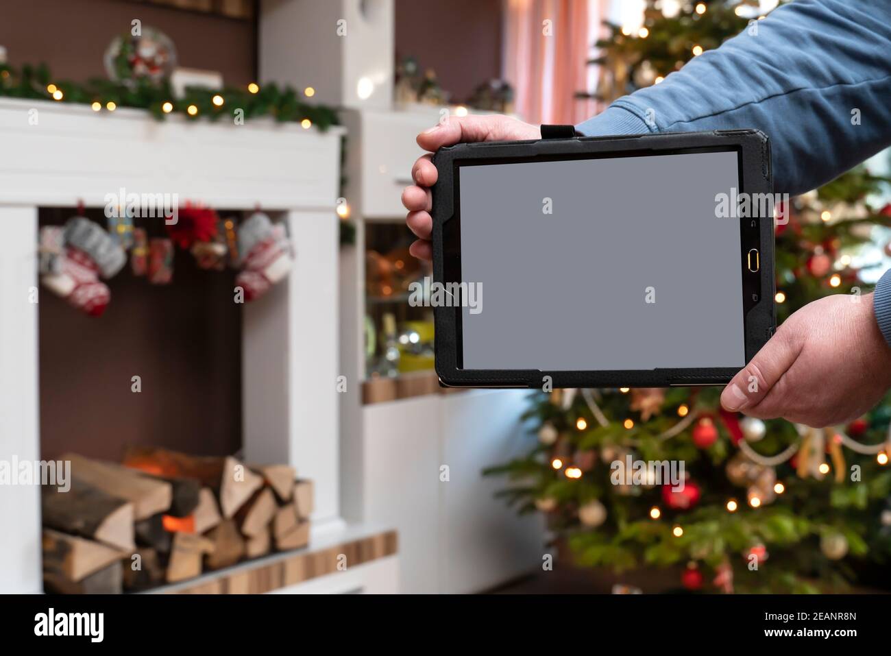 En el apartamento en Navidad un hombre está sosteniendo una bandeja en primer plano es el Tablet PC con espacio de copia. En el fondo está Bokeh del árbol de Navidad. Foto de stock