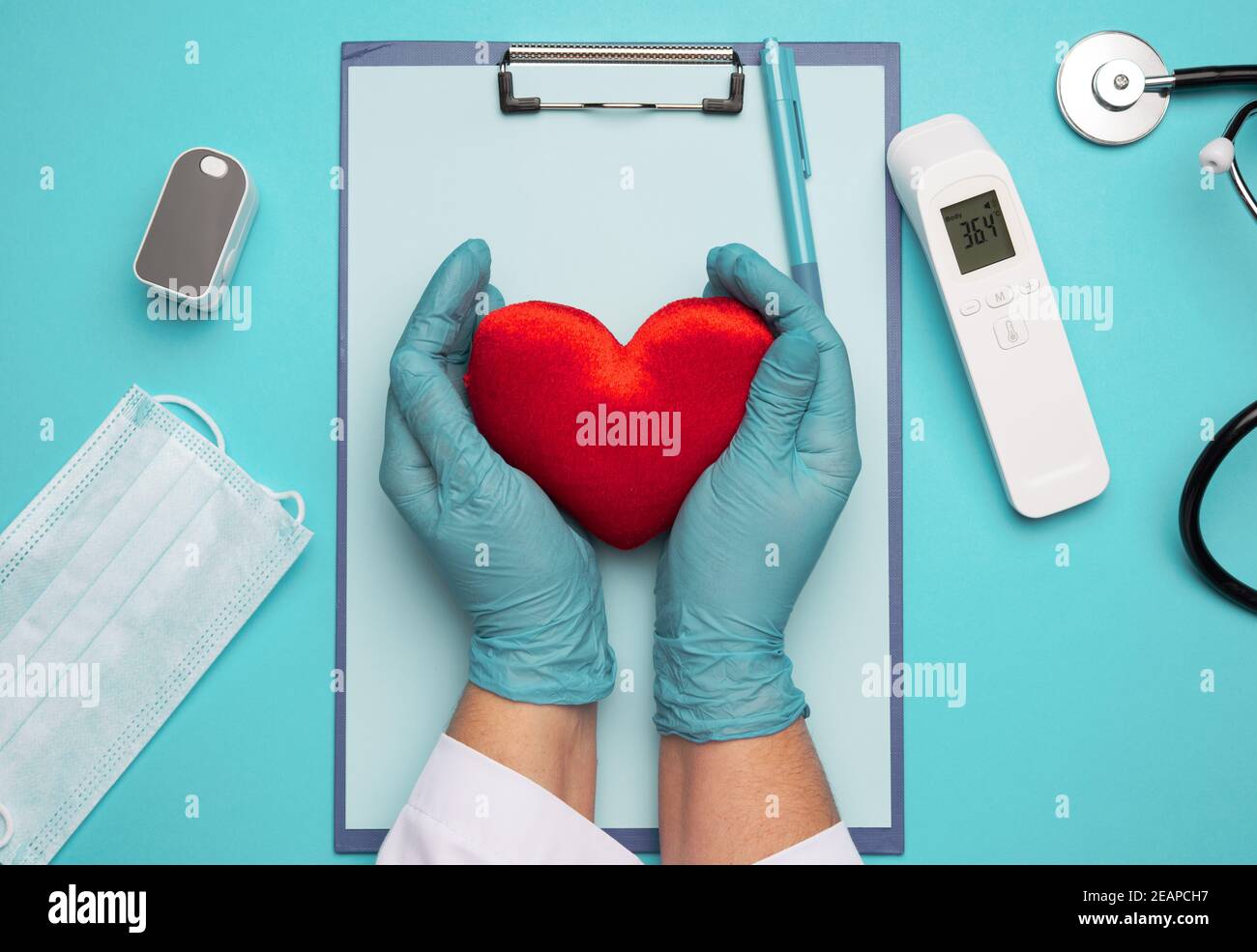dos manos en guantes de látex azul sosteniendo un corazón textil rojo, concepto de donación Foto de stock