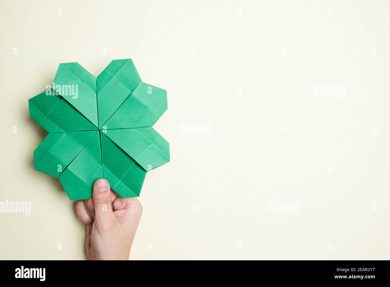Chamrock de cuatro hojas hecho de papel, origami, sostenido por una mano de  una joven sobre un fondo claro. Conceptos de suerte y día de San Patricio.  Imagen con c Fotografía de