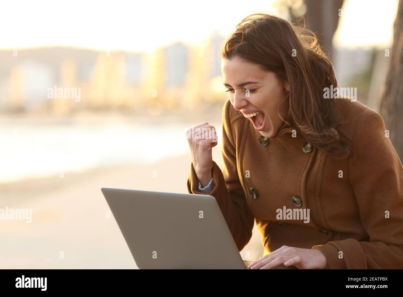 Mujer emocionada leyendo buenas noticias en el portátil en invierno Foto de stock