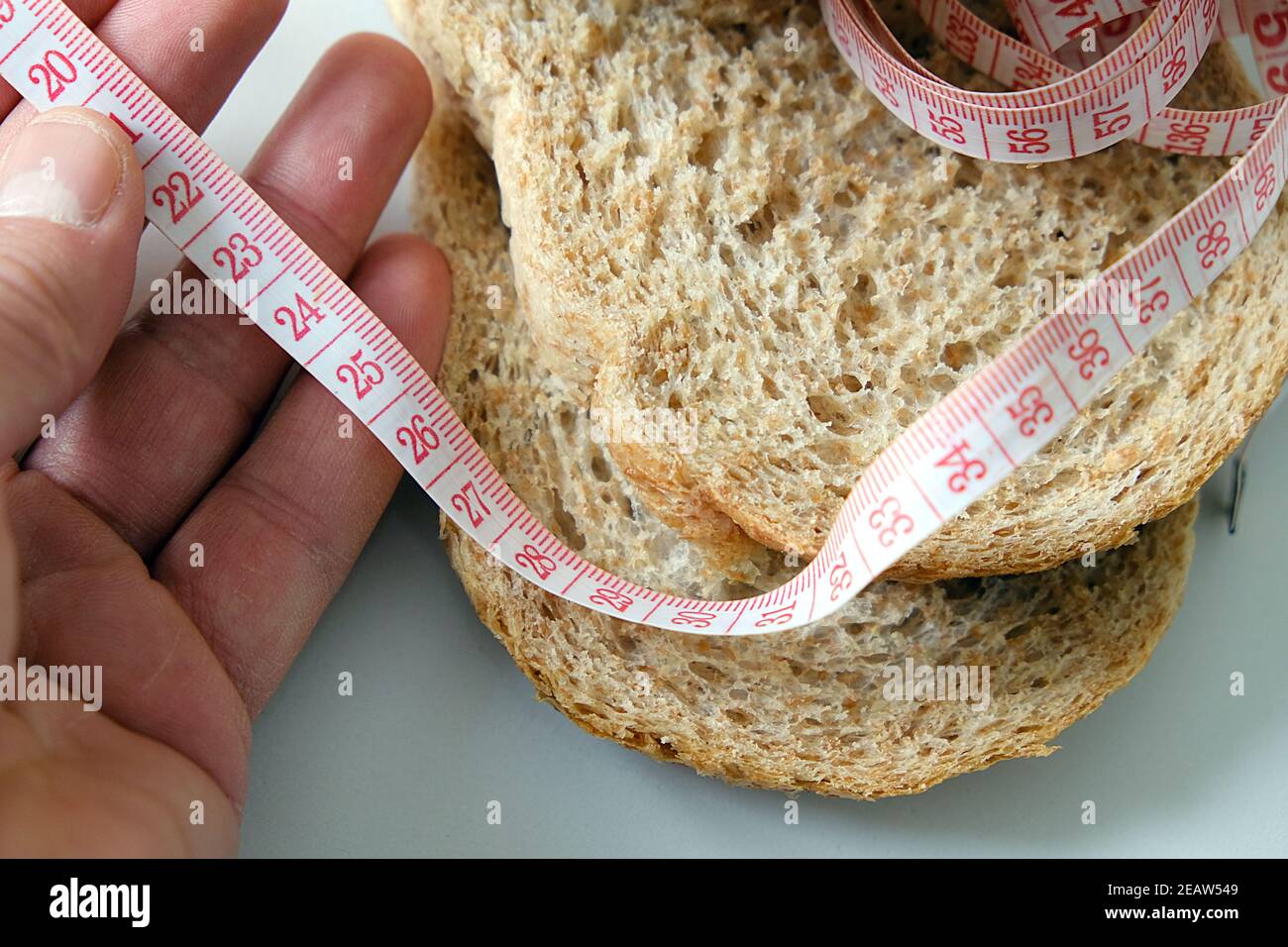 Contra el aumento excesivo de peso en casa, pan de salvado, rebanadas de pan de salvado y una cinta métrica Foto de stock