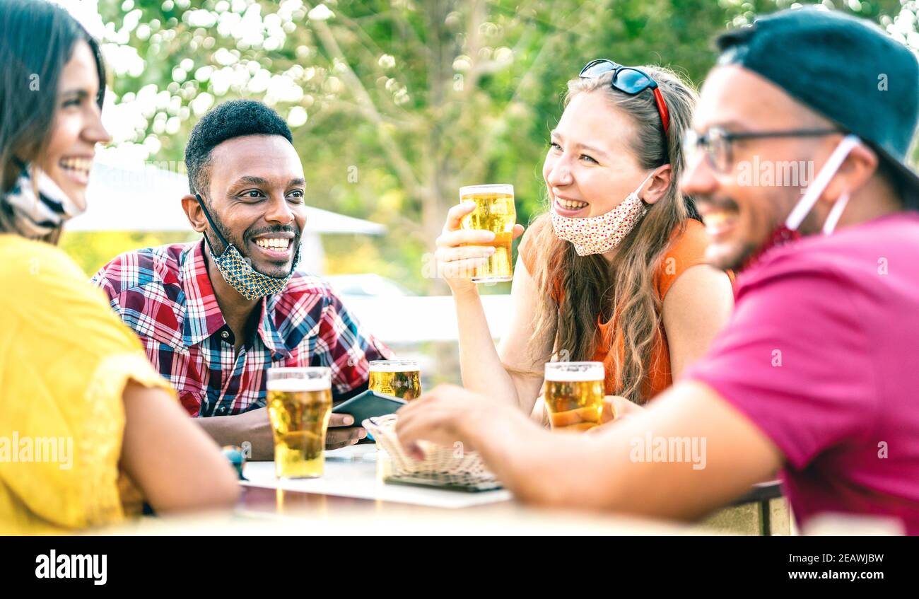 Amigos bebiendo cerveza con máscaras abiertas - Nueva normal concepto de estilo de vida con personas que se divierten juntos hablando de feliz hora en el bar de la fábrica de cerveza Foto de stock