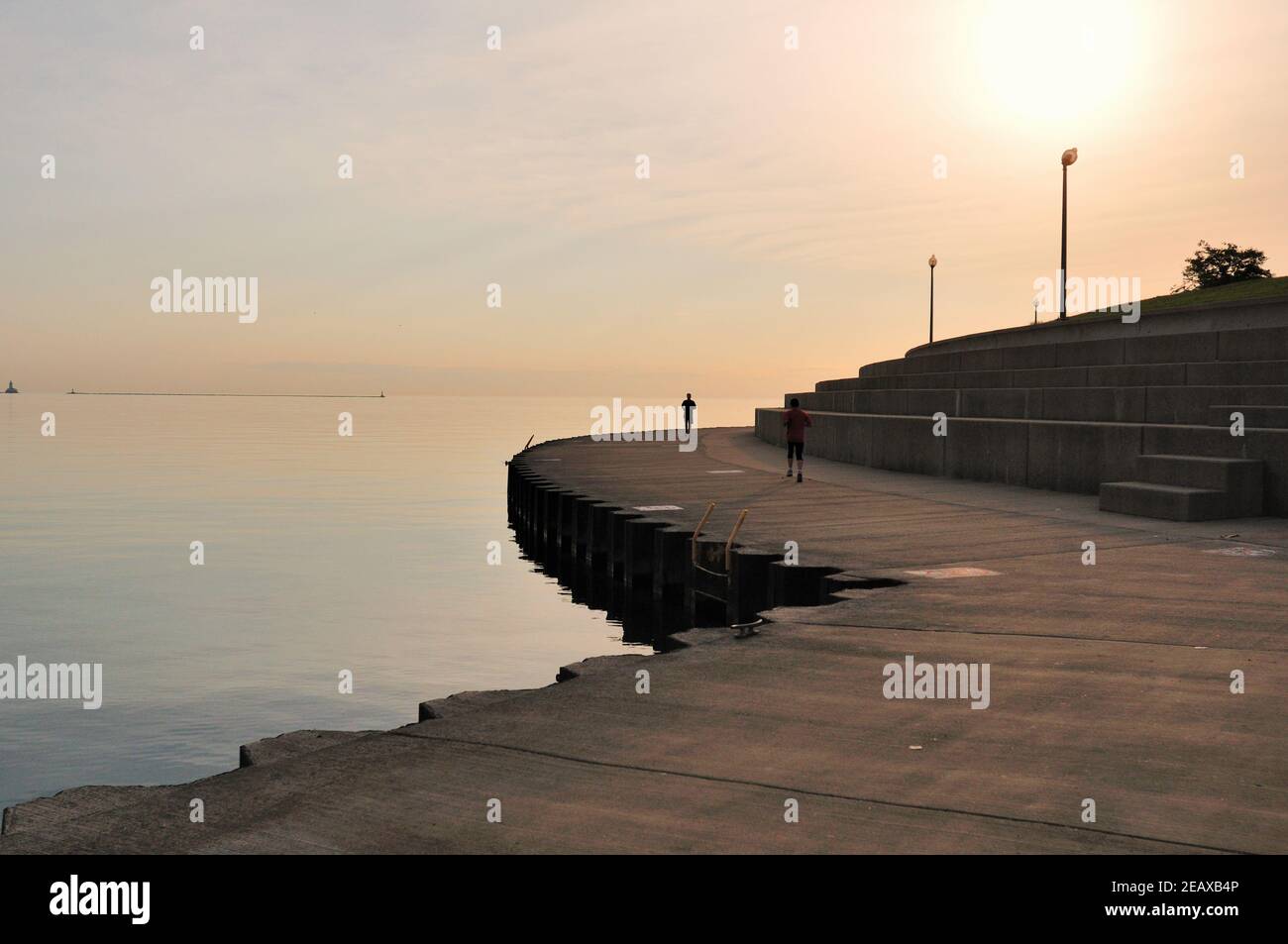 Chicago, Illinois, EE.UU. Dos solitarios joggers corren hacia el amanecer a lo largo de las orillas del Lago Michigan a lo largo de la pared del lago en el Campus de los Museos. Foto de stock