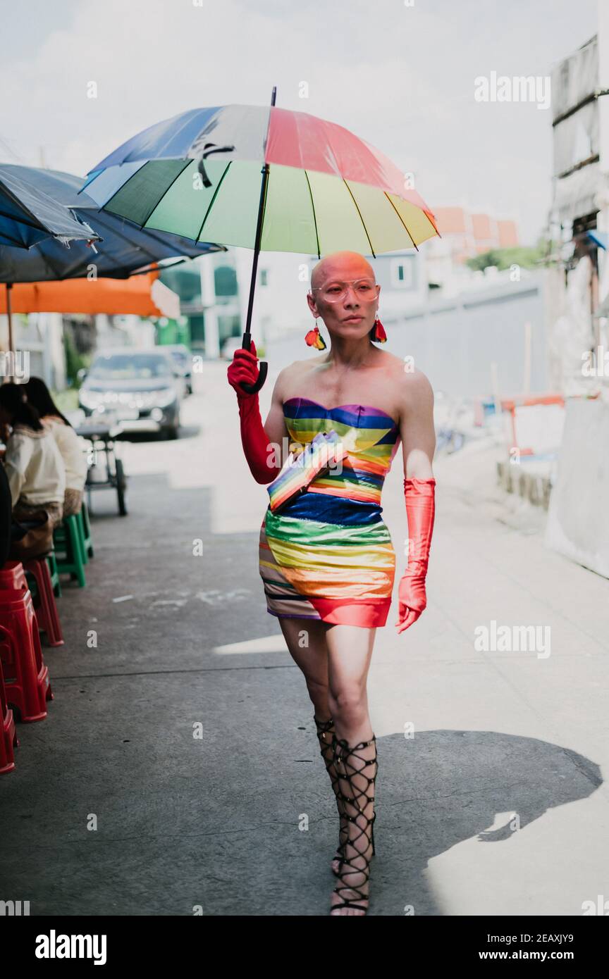Retrato de una persona de la reina asiática vestida con vestido de colores arcoiris, con guantes rojos y sosteniendo un paraguas de colores arcoiris en Bangkok Tailandia. Foto de stock