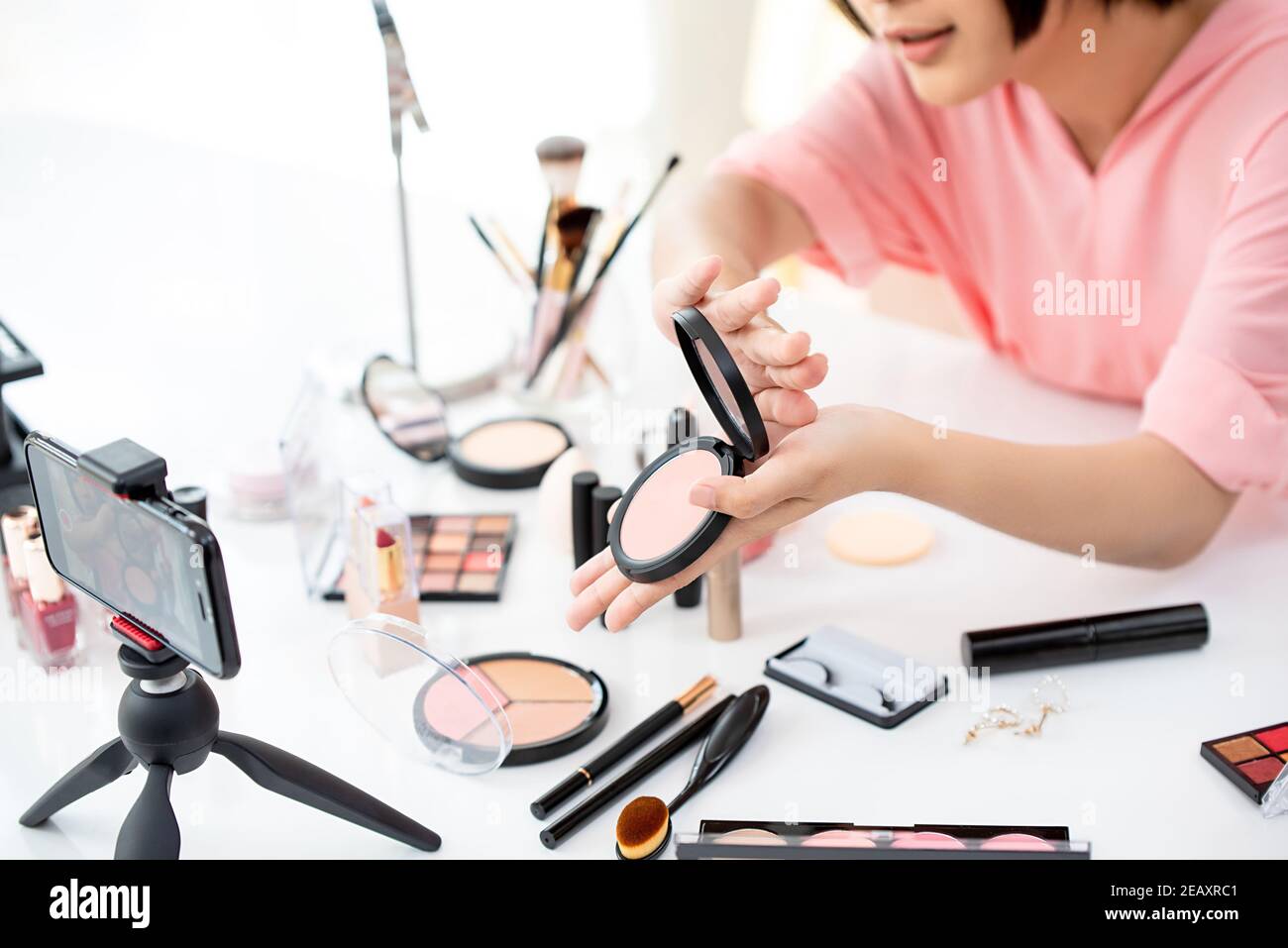Joven vlogger belleza streaming en vivo utilizando el smartphone mostrando productos cosméticos Foto de stock