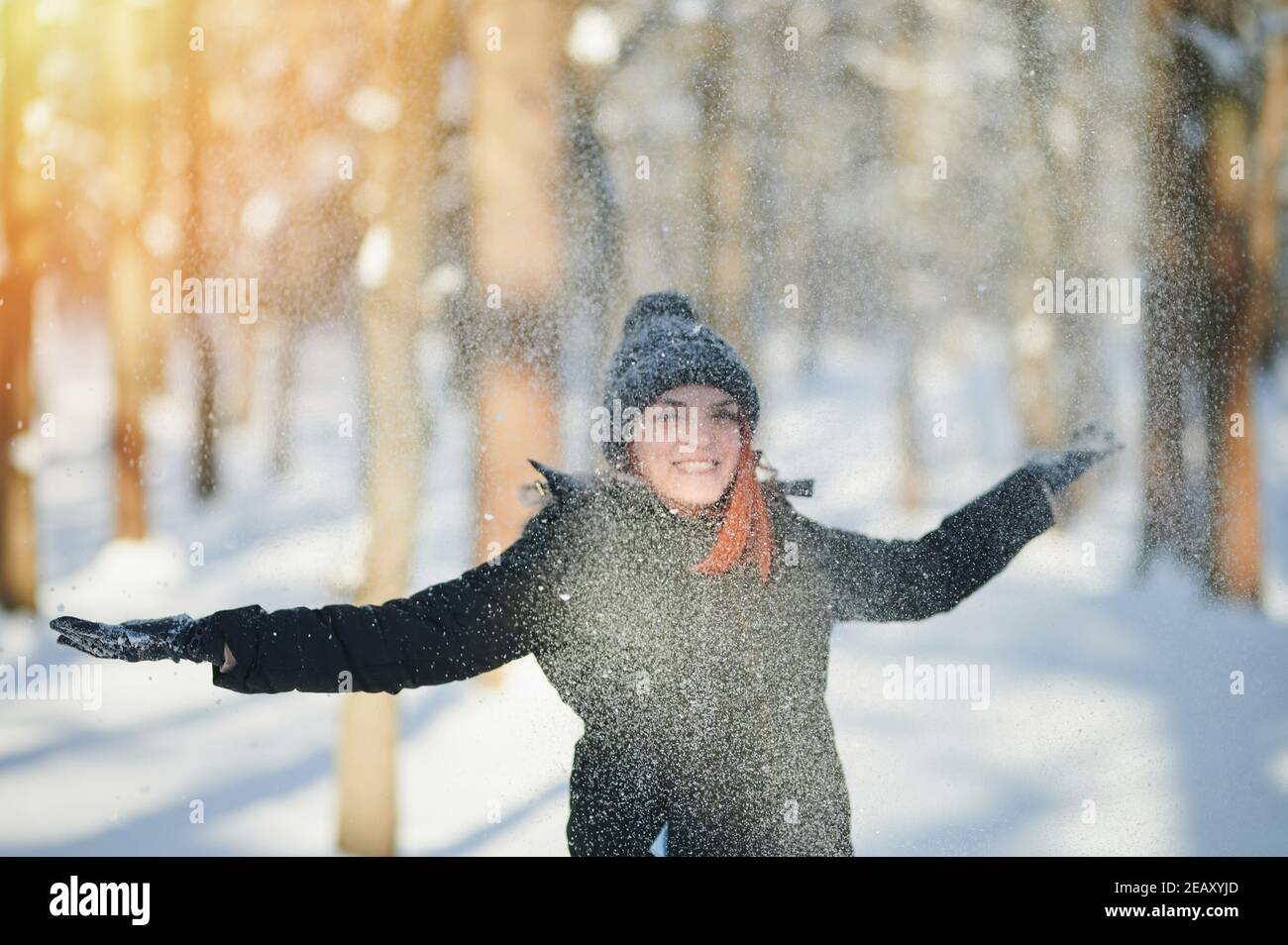 Mujer joven y feliz arrojan nieve en el parque soleado de invierno Foto de stock