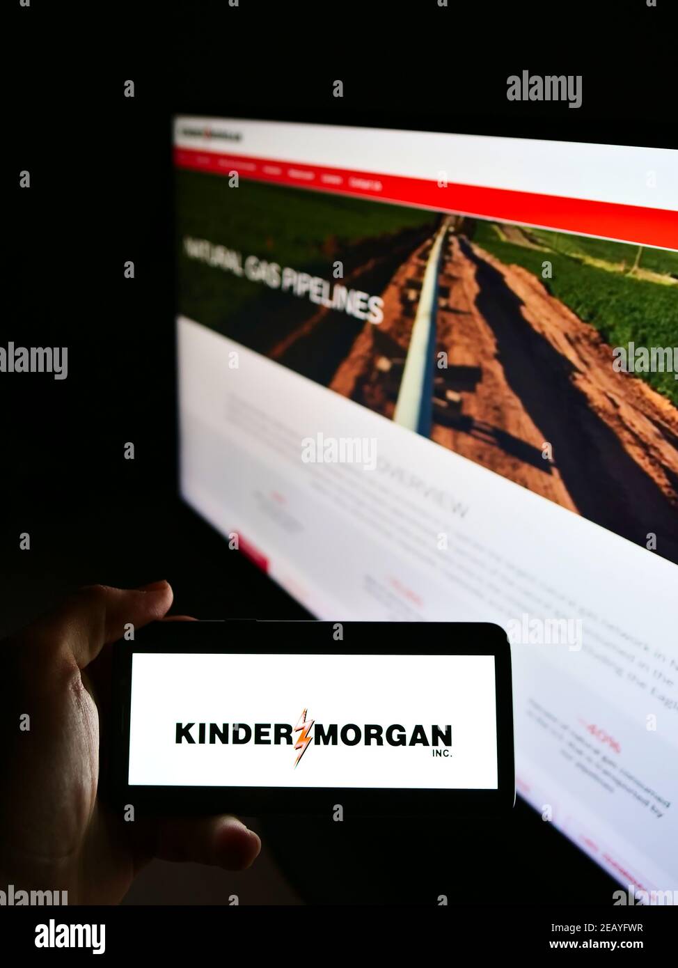 Persona que sostiene el teléfono celular con el logotipo de la empresa estadounidense de infraestructura energética Kinder Morgan Inc. En la pantalla al frente de la página web. Enfoque en la pantalla del teléfono. Foto de stock