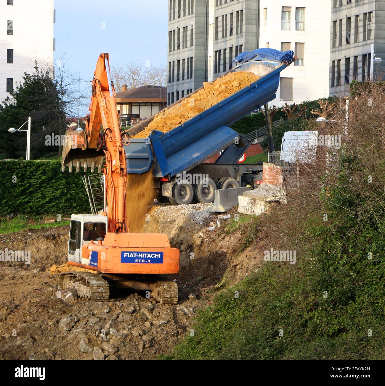 3 de 6 camión volquete azul vaciando arena en un Nueva construcción con un digger naranja Fiat-Hitachi esperando Muévala Santander Cantabria España Foto de stock