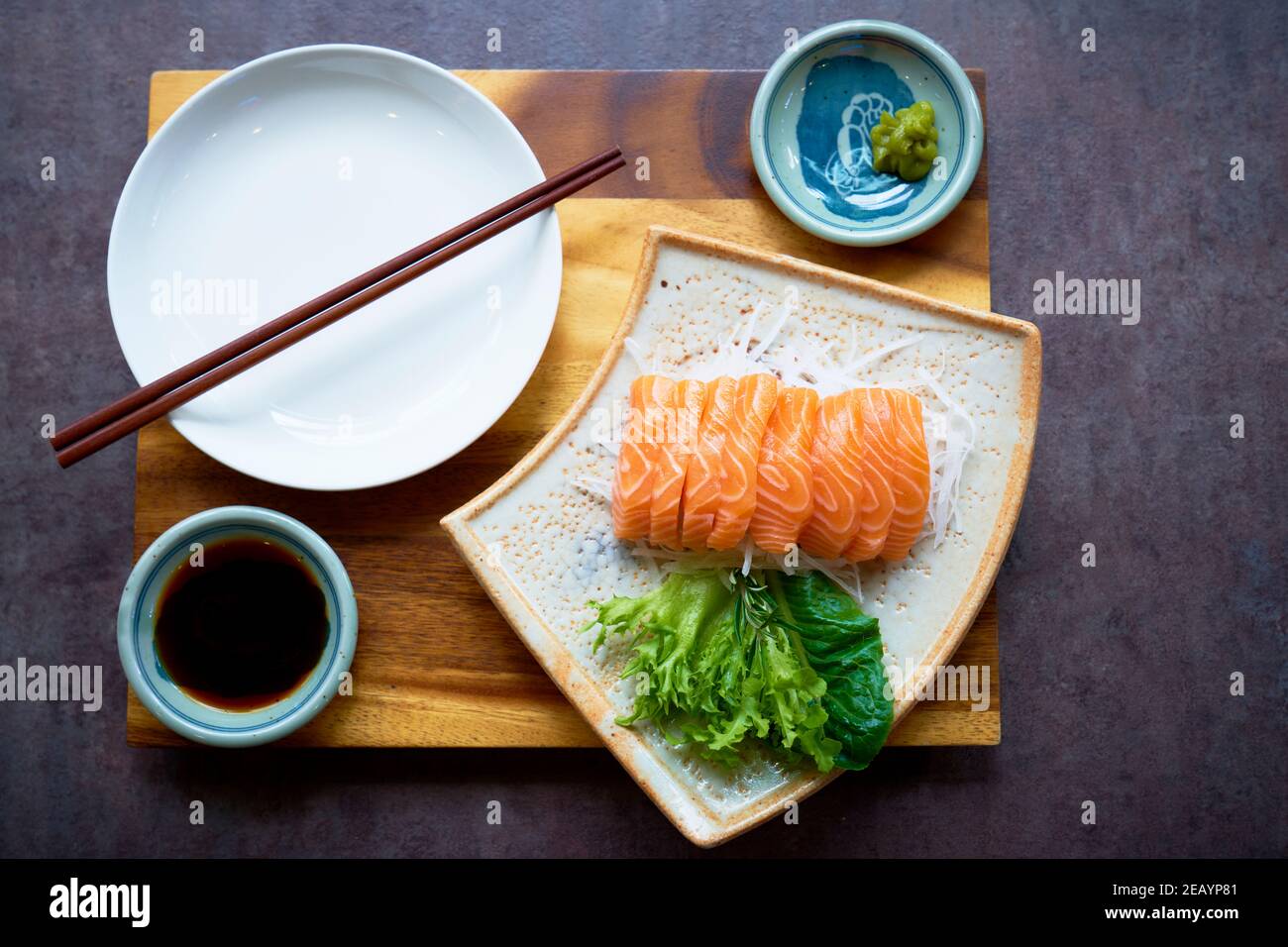 Sashimi de salmón con salsa de soja en arroz con ensalada presentada en un tablero de madera con palillos. Foto de stock