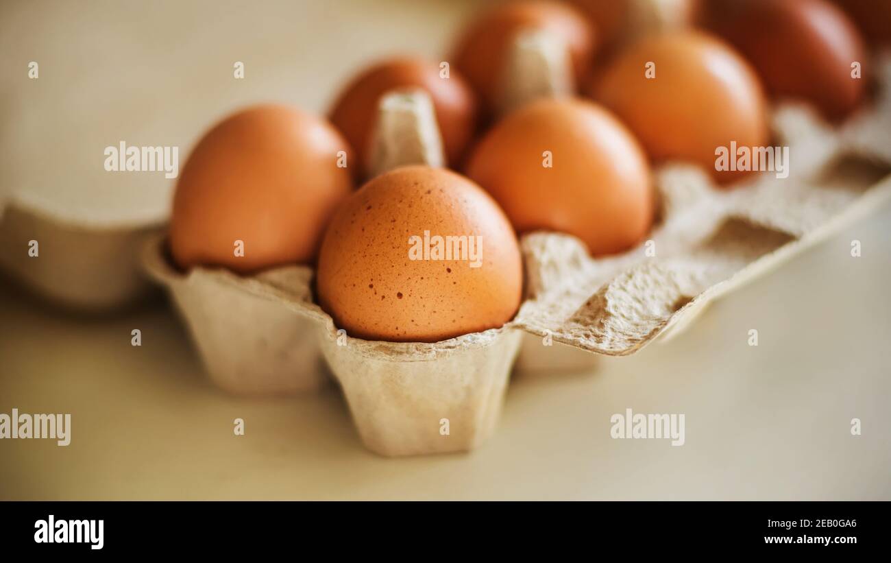 Los huevos de pollo marrones se encuentran en una caja de cartón, están en una mesa blanca e iluminados por la luz del sol. Comida saludable para el desayuno. Foto de stock