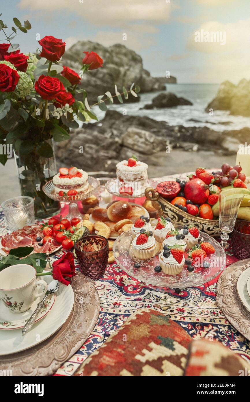 Romántico arreglo de postres variados y frutas frescas con rosas en un  picnic en la playa Fotografía de stock - Alamy