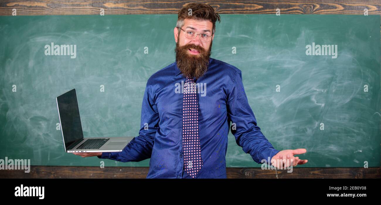 La enseñanza de las cuestiones utilizando las más modernas tecnologías. Profesor Hipster expresión confusa tiene portátil. Maestro hombre barbado confundirse trabajo portátil moderno con pizarra de fondo. Temas de educación a distancia. Foto de stock