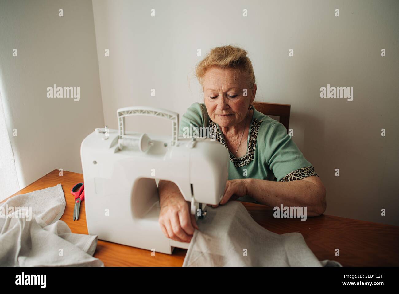 Mujer anciana trabajando en máquina de coser mientras estaba sentada en casa Foto de stock