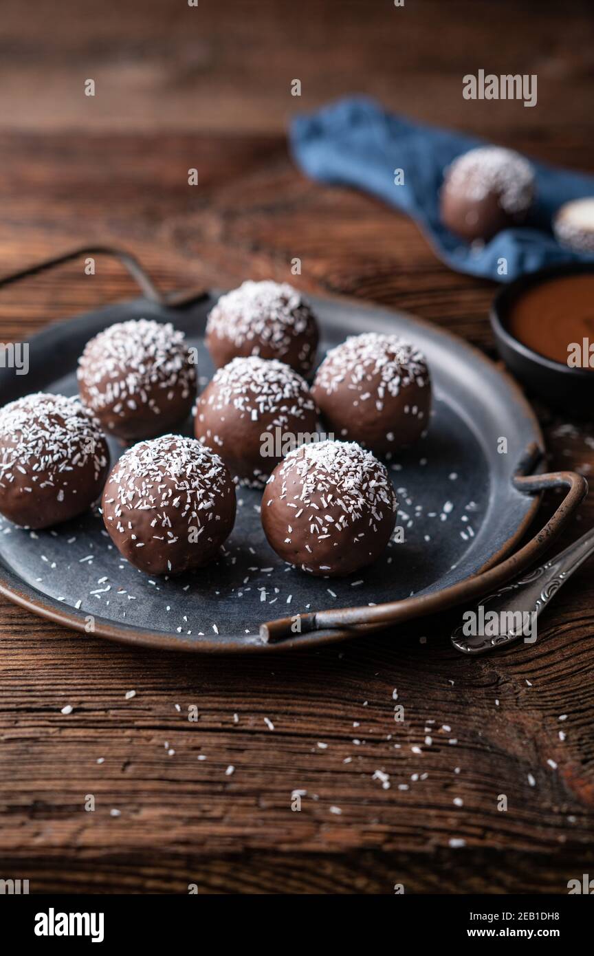 No hornear dulces deliciosos, bolas de coco dulce bañadas en chocolate sobre fondo de madera rústica Foto de stock