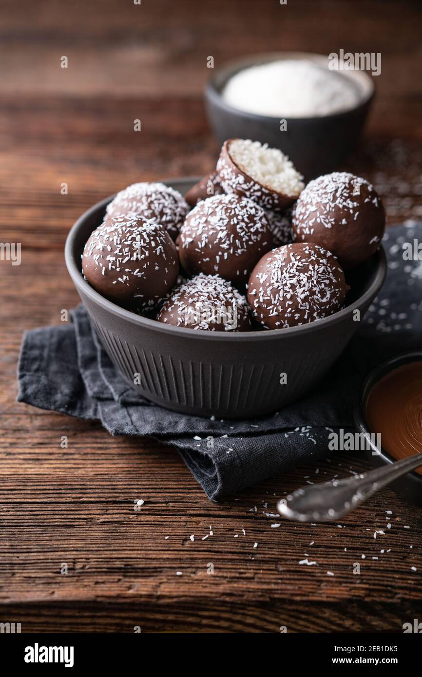No hornear dulces deliciosos, bolas de coco dulce bañadas en chocolate sobre fondo de madera rústica Foto de stock