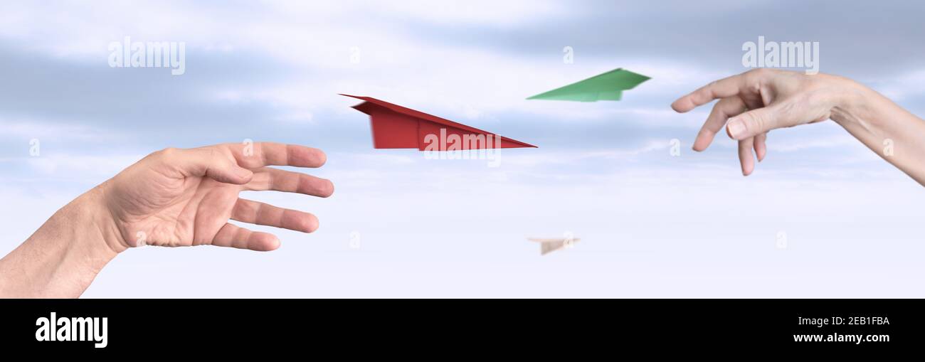 Dos manos (hombre, mujer) lanzan aviones de papel multicolores, fondo del cielo. Foto de stock