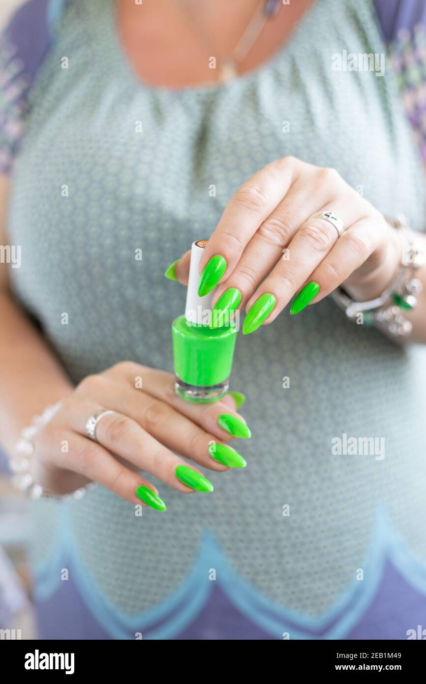 Mano femenina con uñas largas y manicura verde neón con botellas de esmalte  de uñas Fotografía de stock - Alamy