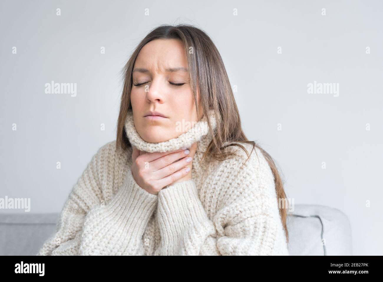 Mujer joven en un suéter acogedor tocando el cuello doloroso. Dolor de garganta, inflamación de la garganta. Síntoma de coronavirus Foto de stock