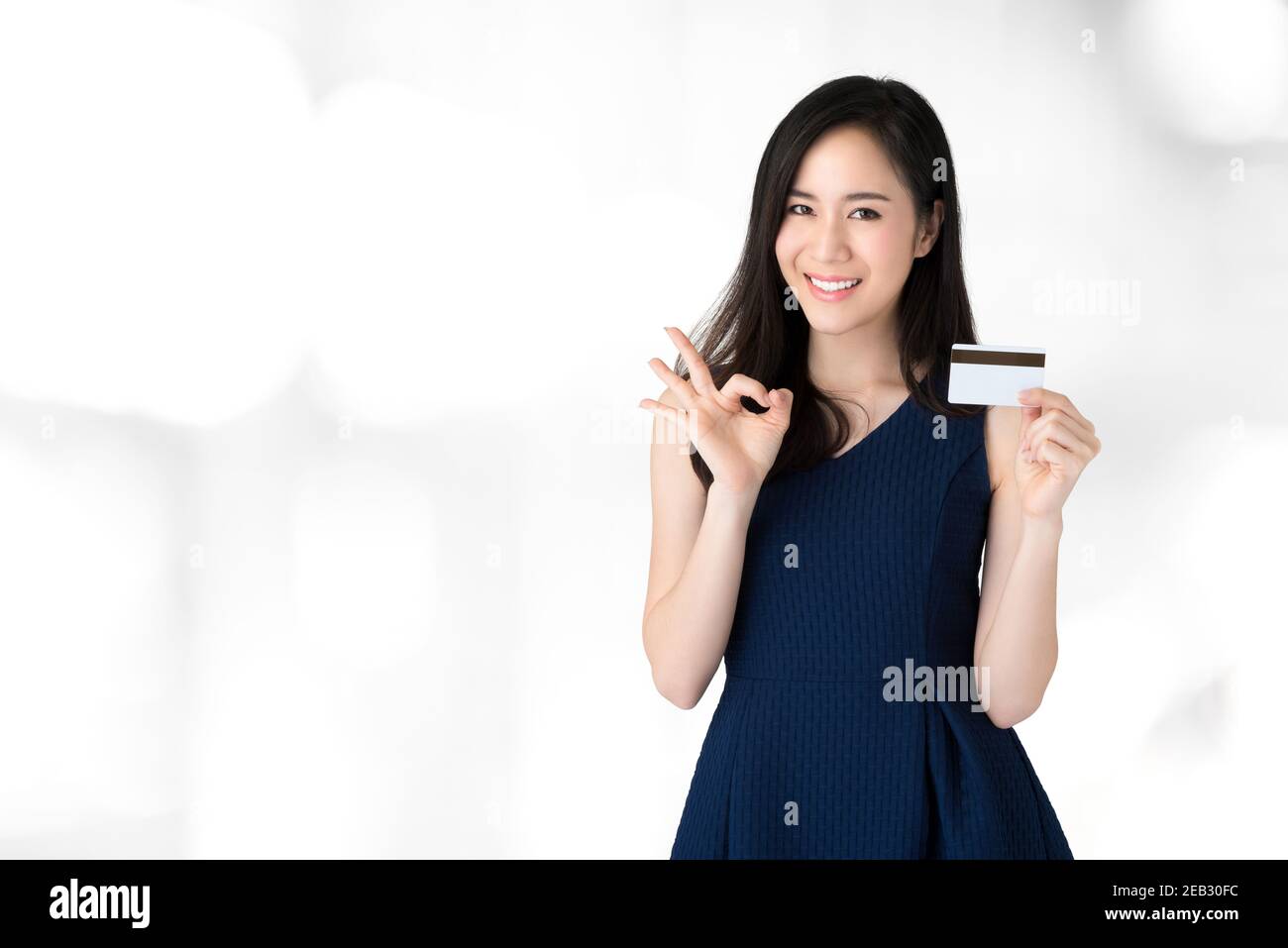 Joven sonriente hermosa mujer asiática mostrando tarjeta de crédito con okey gesto Foto de stock