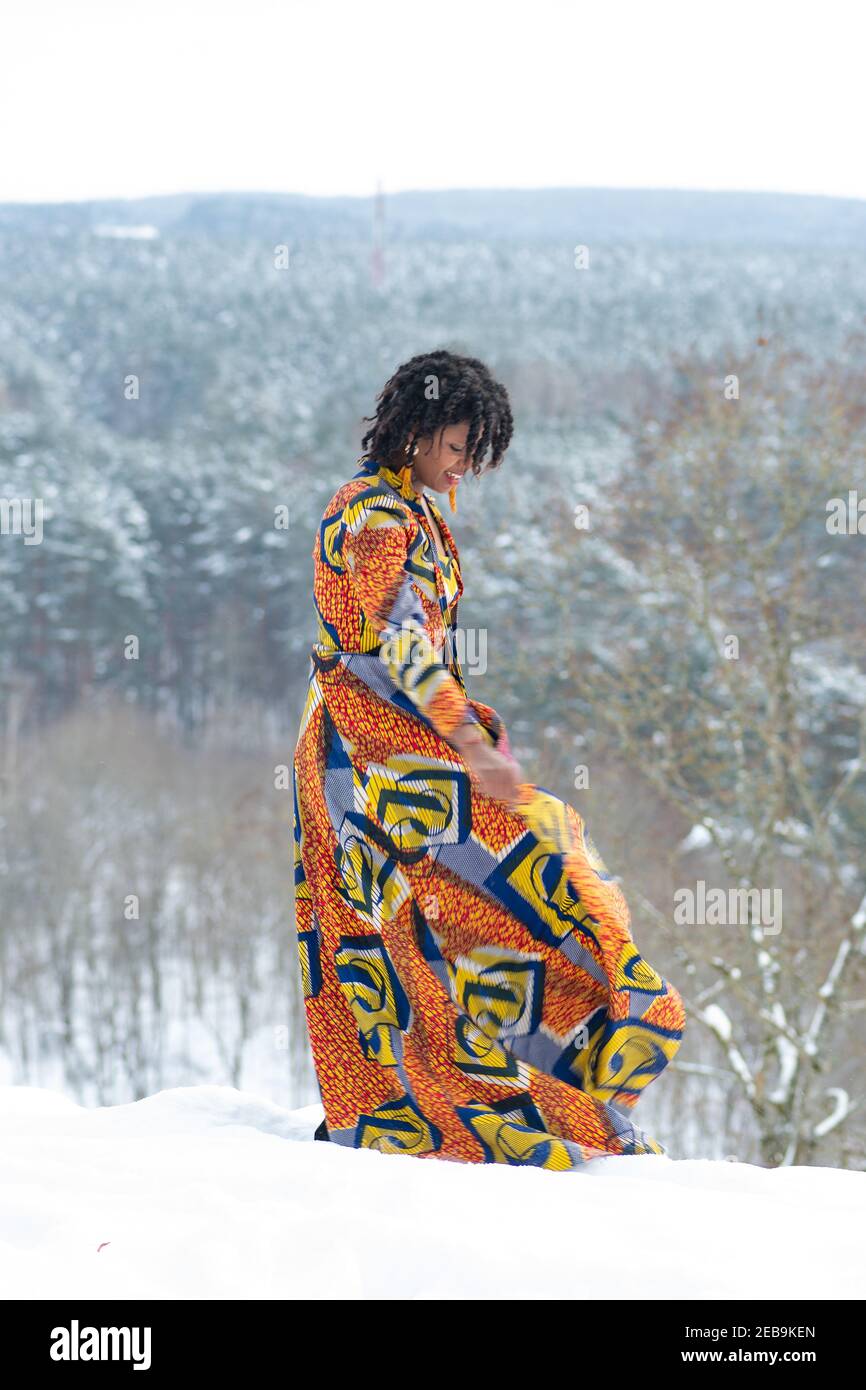 Hermosa chica con vestido de colores bailando en la nieve en invierno con árboles forestales cubiertos de nieve en el fondo, vertical Foto de stock