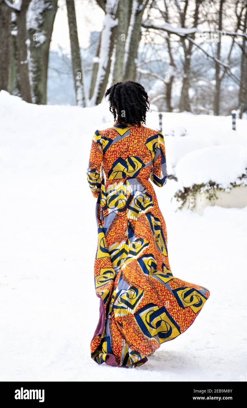 Hermosa chica con vestido de colores caminando sobre la nieve en invierno con árboles forestales cubiertos de nieve en el fondo, vertical Foto de stock