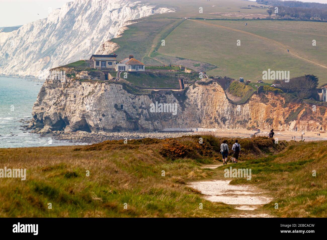 Escarpada costa de la Isla de Wight con la bahía de Freshwater, promontorios, acantilados y playas. Una pareja os senderismo en la colina en un sendero entre gran gra Foto de stock