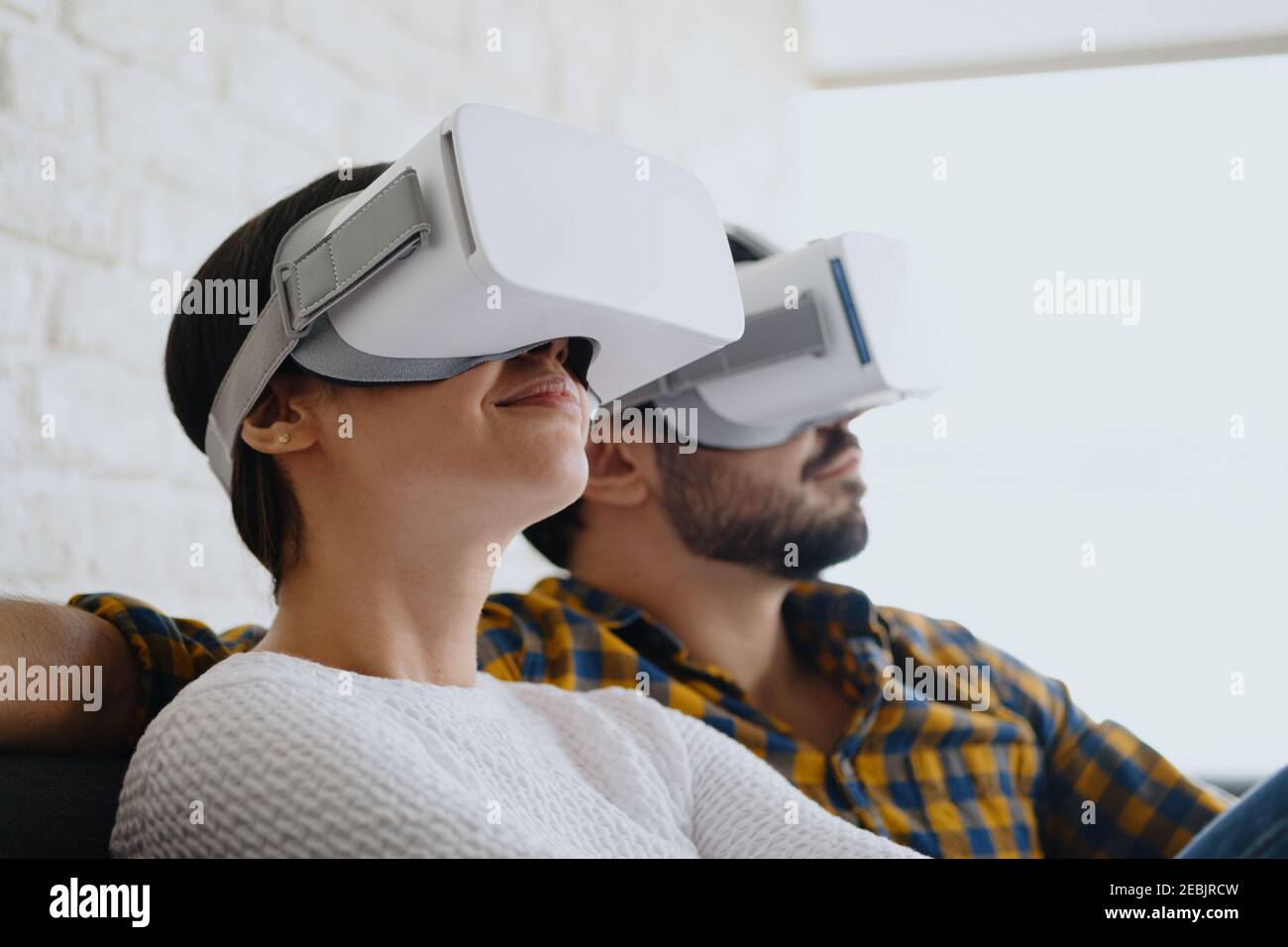 Pareja joven jugando a la realidad Virtual con auriculares en el sofá Foto de stock