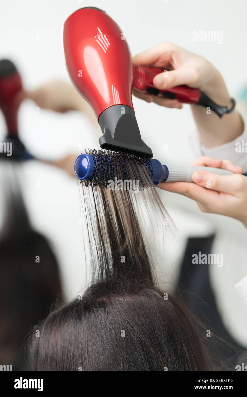 Manos de estilista seca el pelo largo de la morena del cliente usando el  secador rojo y el peine azul en el salón profesional del pelo Fotografía de  stock - Alamy