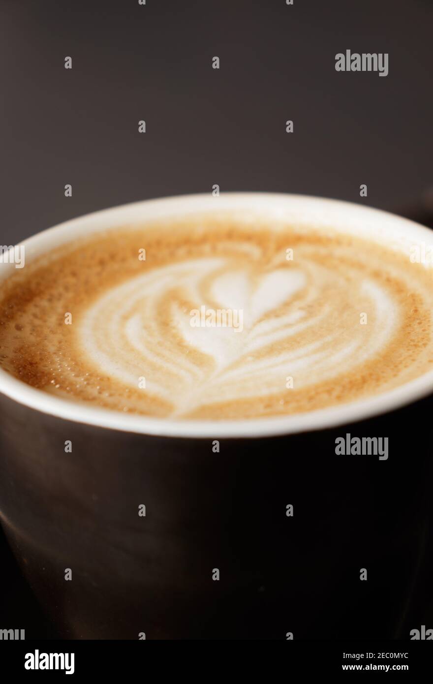 Blanco plano en una taza de café con una flor en forma de corazón dibujado con espuma de leche. Para usar como fondo, enfoque selectivo Foto de stock