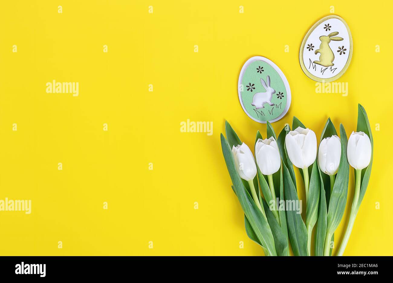 Postal de caballete. Tulipanes blancos y huevos de conejito de madera sobre fondo amarillo Foto de stock