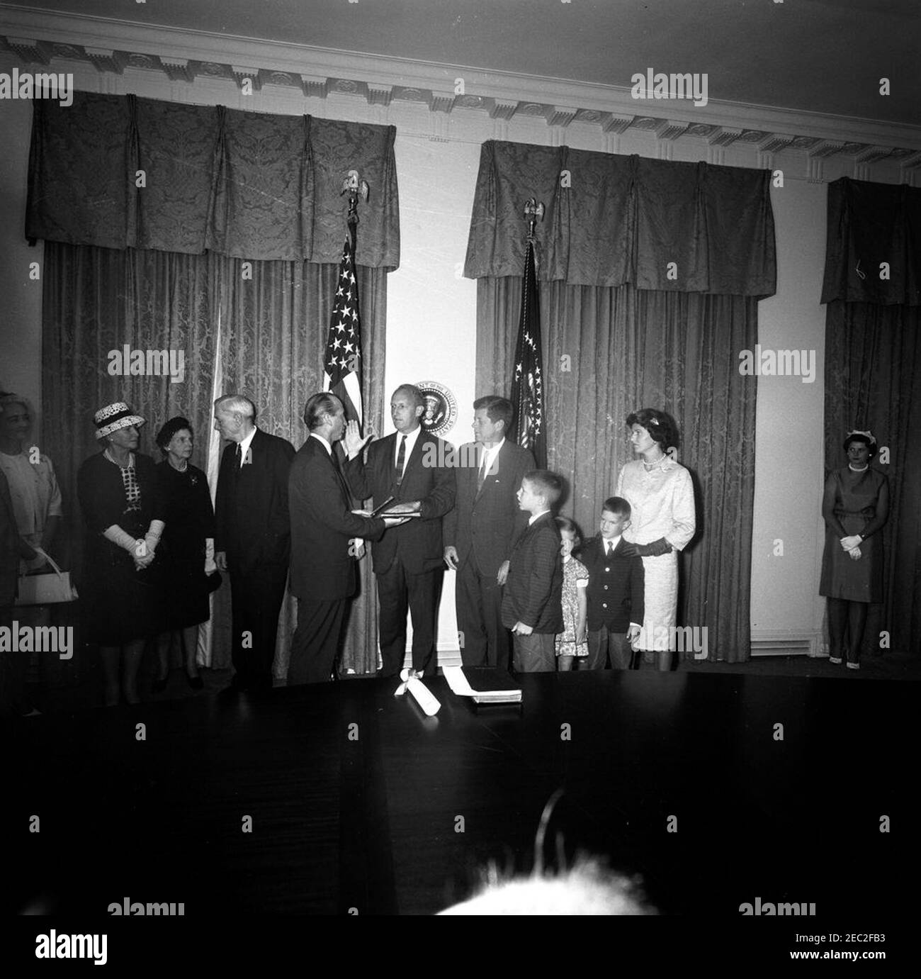 Jurando en la ceremonia, William Battle, Embajador de EE.UU. En Australia, 5:14PM. Ceremonia de juramento del Embajador de los Estados Unidos en Australia, William C. Battle. El Presidente John F. Kennedy mira como Jefe de Protocolo, Angier Biddle Duke (centro izquierda), administra el juramento al Sr. Battle (centro); el ex Gobernador de Virginia, John S. Battle, está a la izquierda del Sr. Duke. También en la foto (a la derecha del Presidente Kennedy): W. Cullen Battle, Jr.; Janie Battle; Robert W. Battle; Barry Webb Battle. Sala del Gabinete, Casa Blanca, Washington, D.C. [fotografía de Harold Sellers] Foto de stock