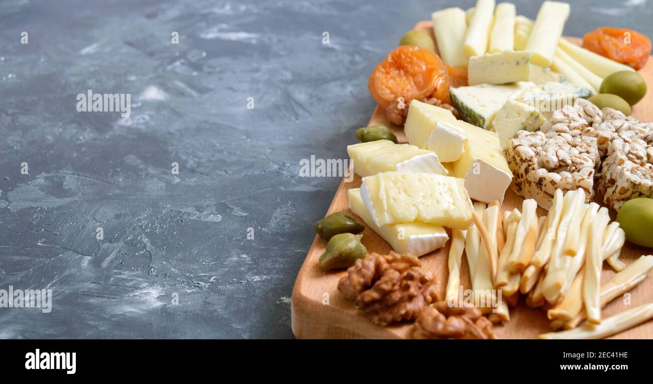 Diferentes tipos de quesos, albaricoques secos, panes integrales, frutos secos, aceitunas, alcaparras en una tabla de madera. Tabla de quesos, aperitivos. Espacio de copia Foto de stock