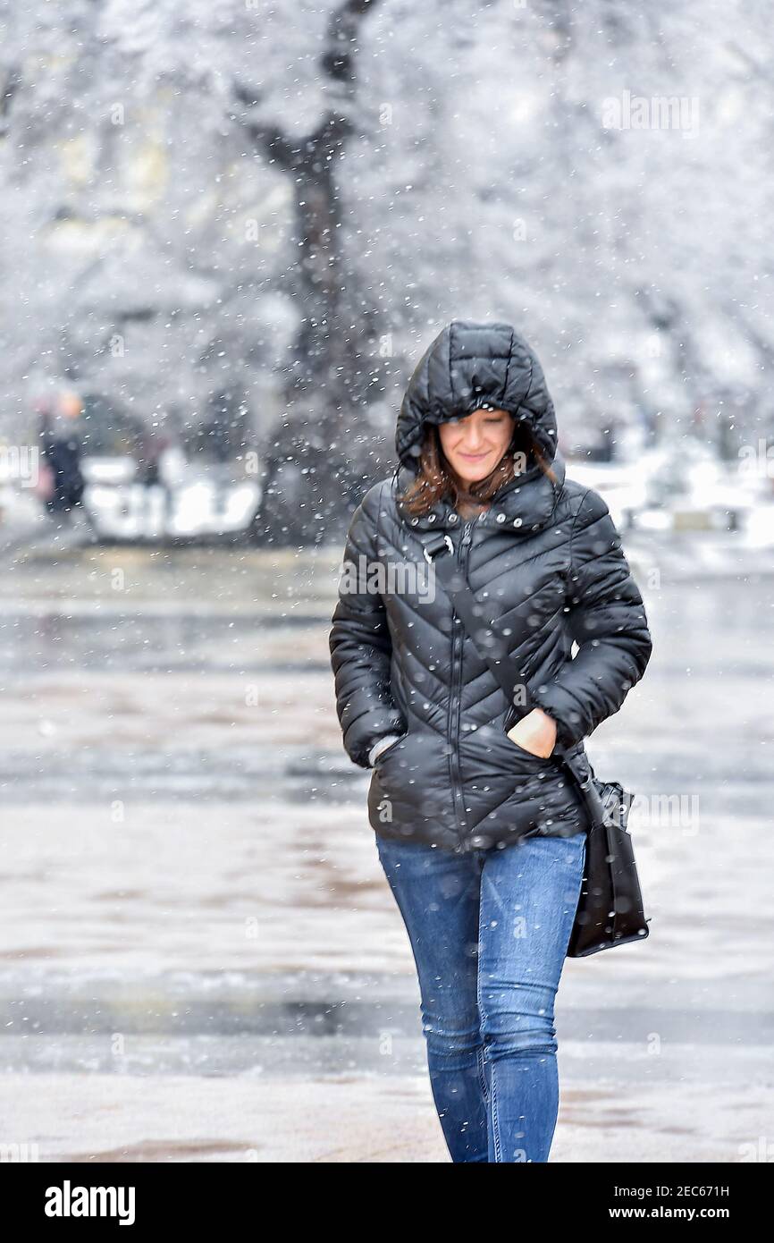Mujer Con Ropa De Invierno Y Sombrero Caminando Al Aire Libre Bajo La Nieve.  Mujer De Pie Bajo La Luz De La Calle Mirando La Nieve Que Cae En La Noche.  País