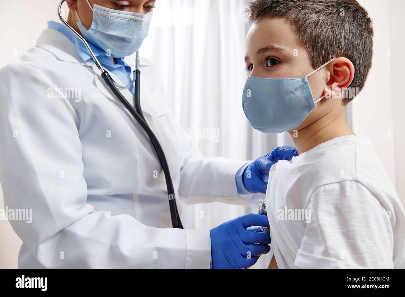 La pediatra femenina en uniforme médico usa un estetoscopio mientras  ausculta un niño en máscara médica protectora Fotografía de stock - Alamy