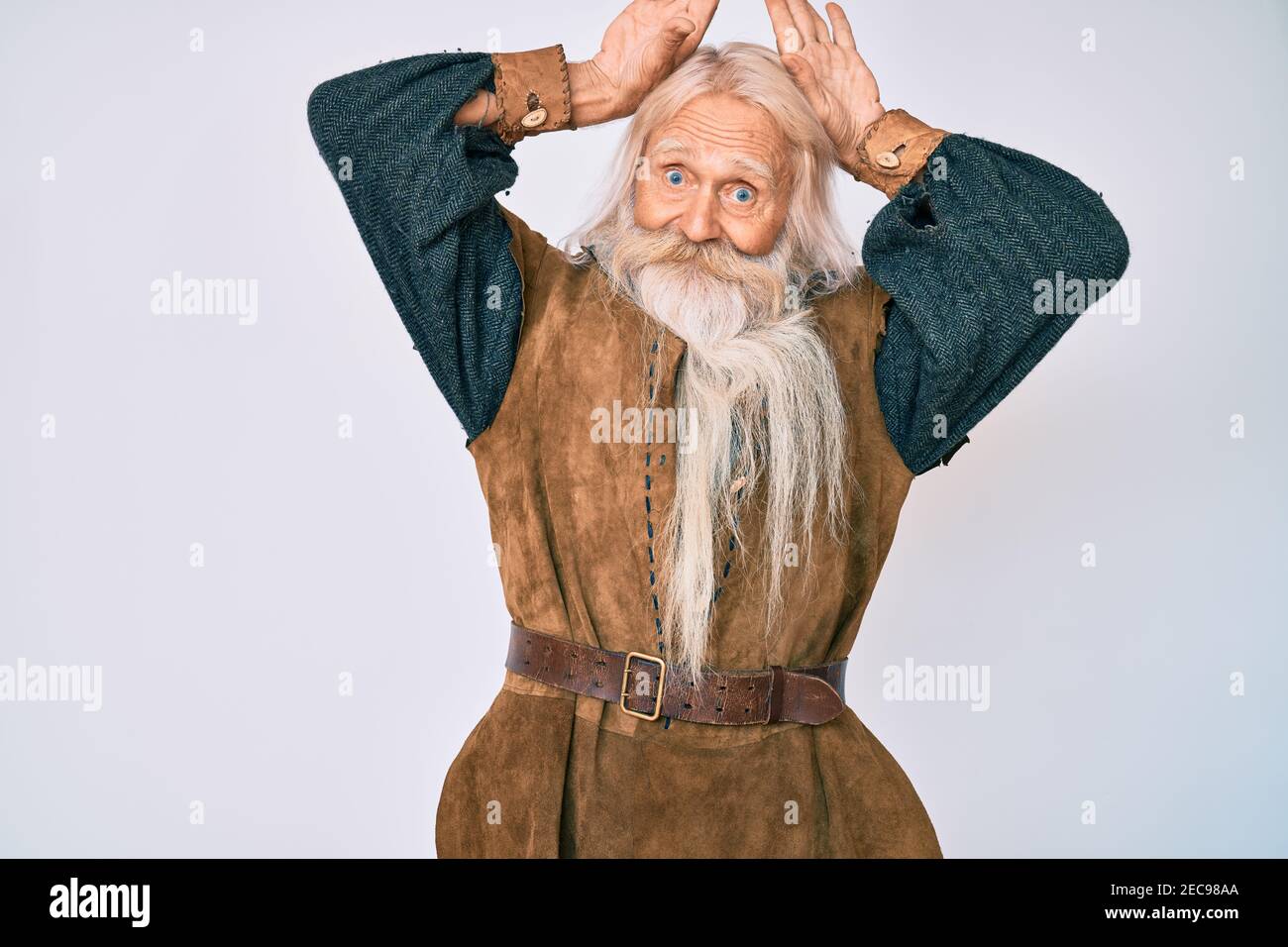 Viejo anciano con pelo gris y barba larga disfraz tradicional vikingo  haciendo el gesto de las orejas de conejito con las palmas de las manos  parece cínico y escéptico Fotografía de stock -