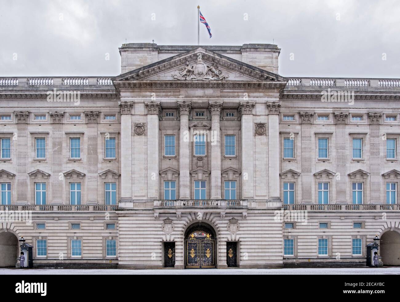 La fachada del Palacio de Buckingham con soldados de Queens Footguard de servicio, nieve de invierno, nubes oscuras, Londres, Reino Unido Foto de stock