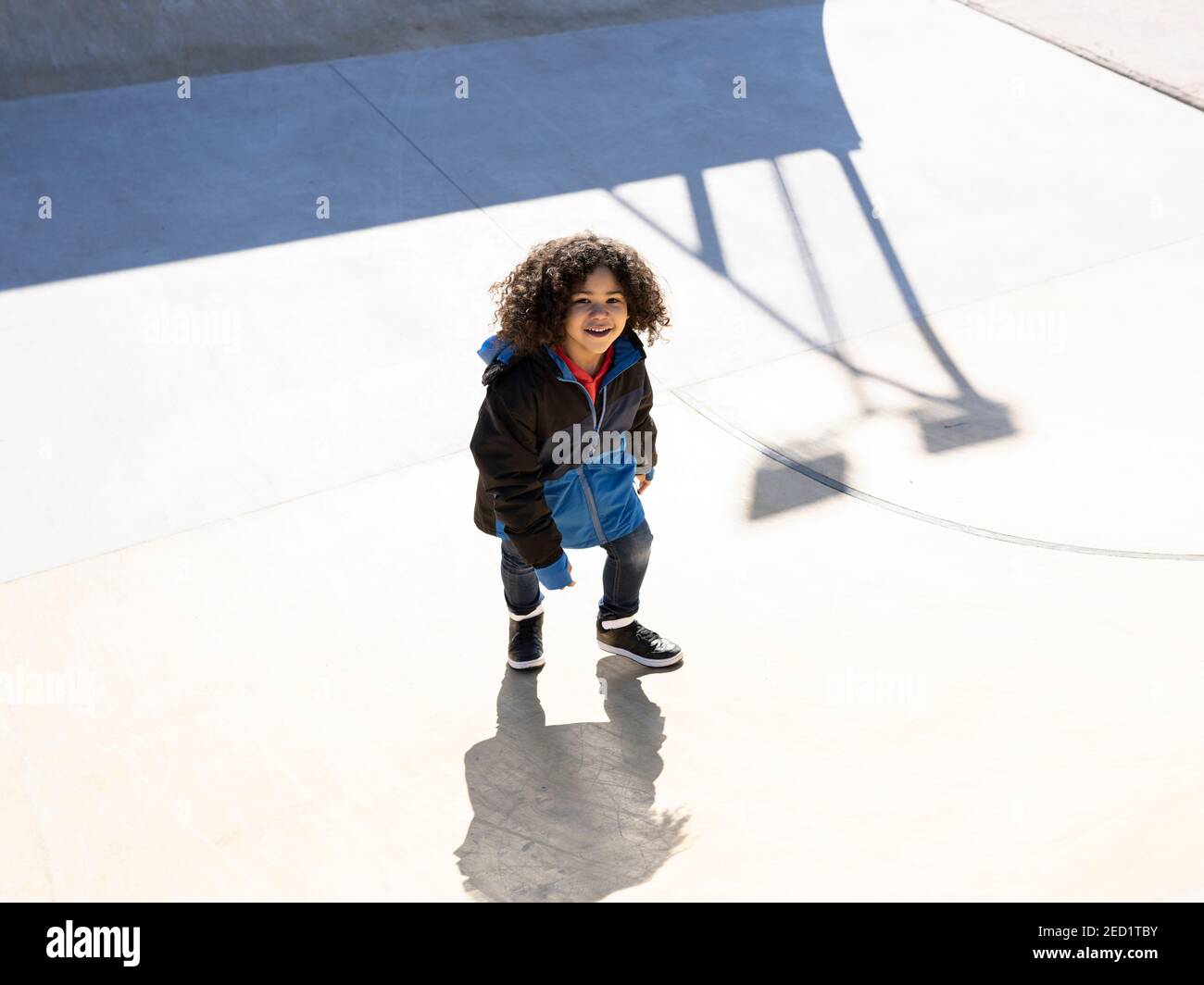 Desde arriba de un niño étnico positivo con peinado afro corriendo sube la rampa mientras te entretiene en el parque de patinaje durante el fin de semana día soleado Foto de stock