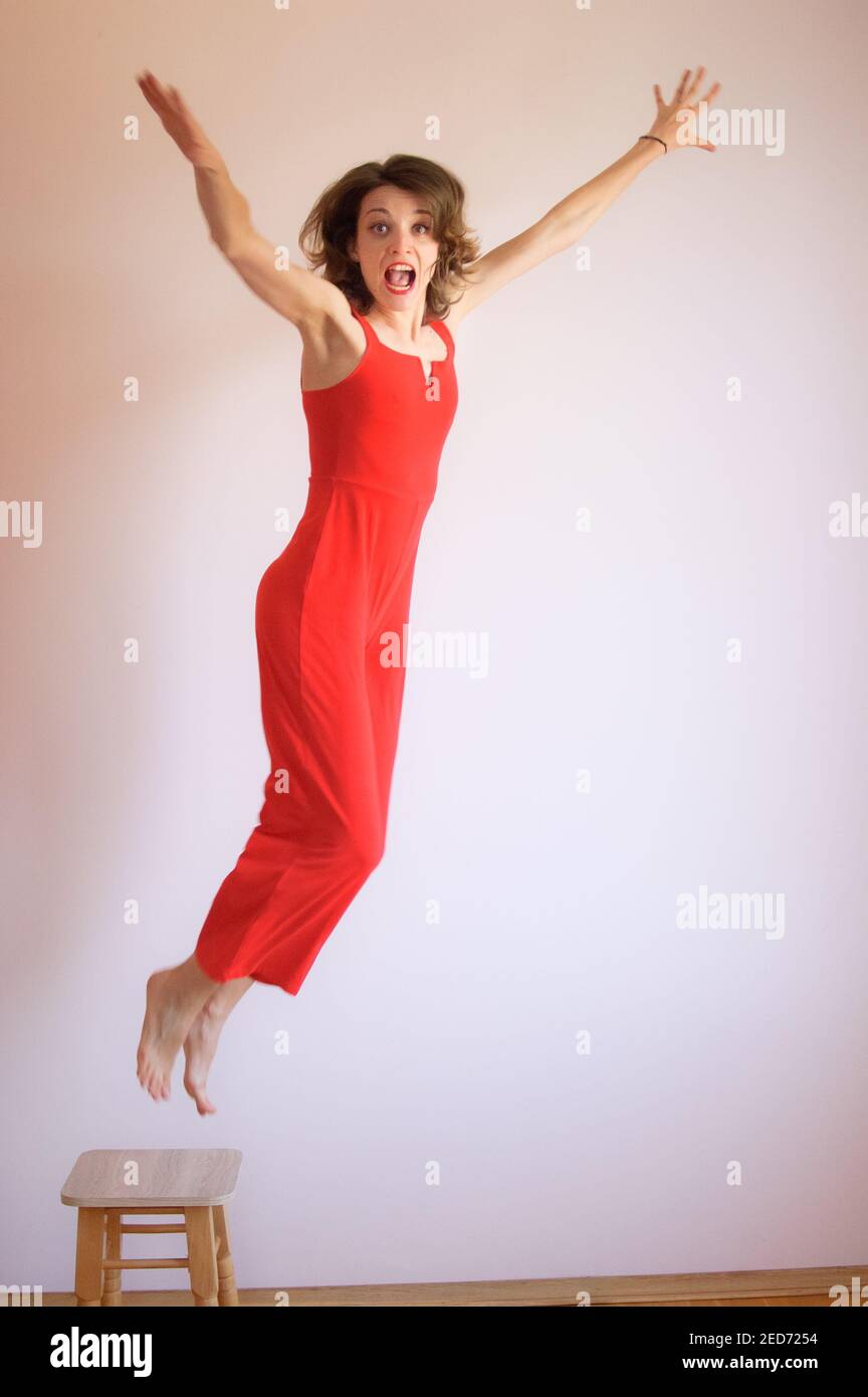 Loco positivo joven morena mujer en overoles rojos saltando de taburete de  madera en casa Fotografía de stock - Alamy