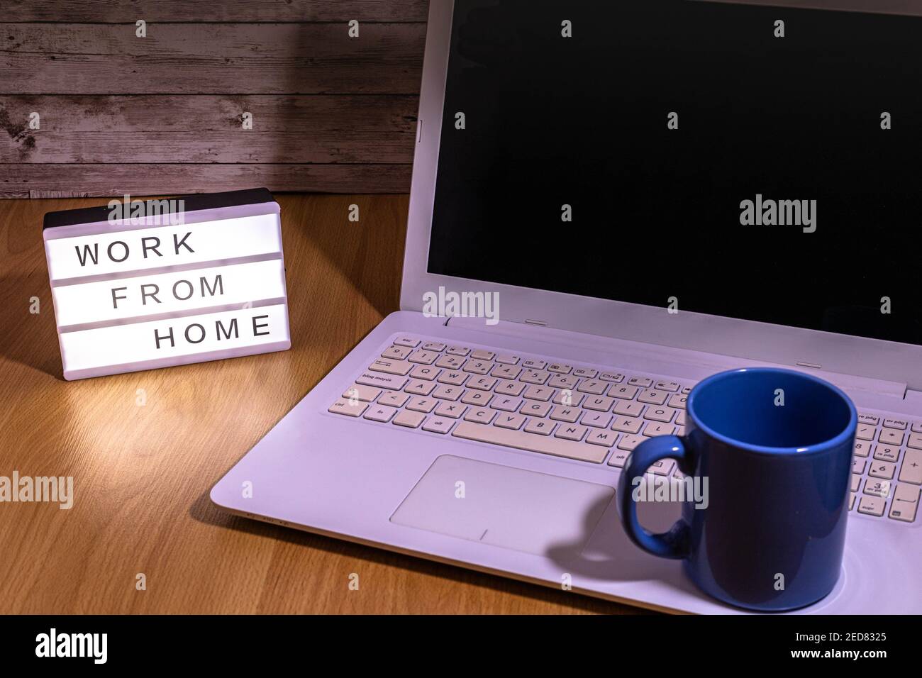 taza de café azul colocada en la parte superior del portátil Con una caja de luz que indica el trabajo desde casa por social distancia en tiempo de concepto de salud de covid19 Foto de stock