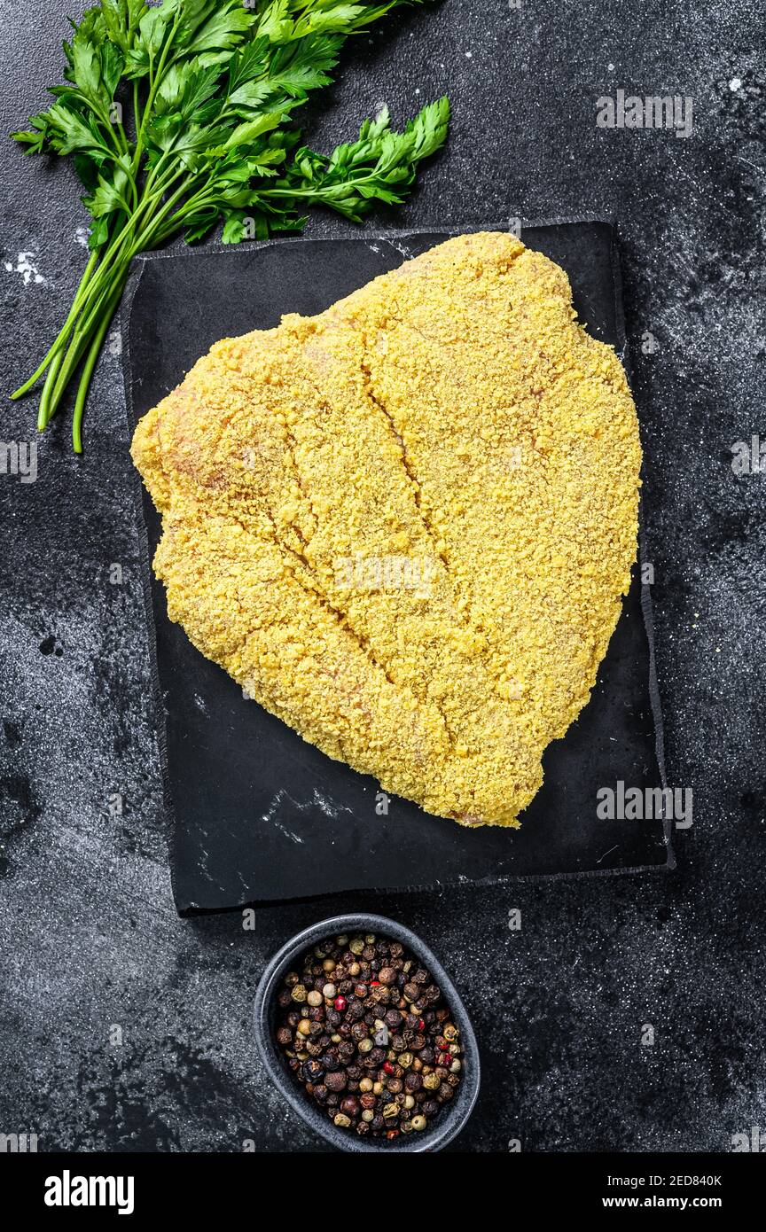 Schnitzel vienés grande crudo en una tabla de corte. Fondo negro. Vista superior Foto de stock