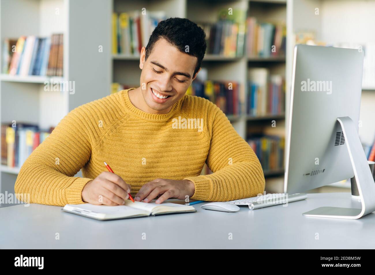 Aprendizaje en línea. Un joven hispano atractivo aprende en línea a través de una videollamada, toma nota de la información durante la lección mientras está sentado en el escritorio de trabajo Foto de stock