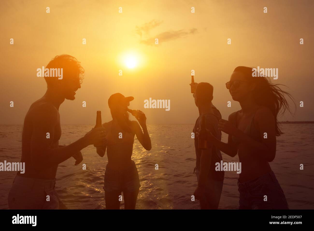 Grupo de amigos que tienen fiesta celebrando y bebiendo en el playa en verano puesta de sol crepúsculo Foto de stock