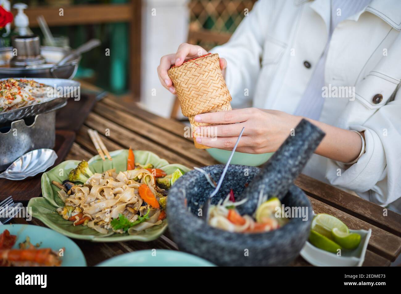 Mujer abriendo un recipiente pegajoso de bambú de arroz mientras que teniendo un tres Plato de comida en un restaurante tailandés closeup Foto de stock