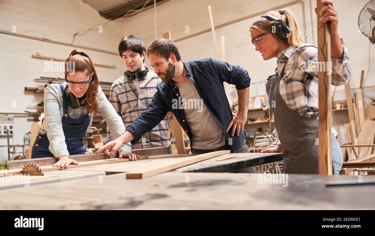 Carpenter aprendices con entrenadores en la sierra circular en el taller de carpintería Foto de stock